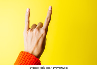 Woman's Hand In Red Sweater Shows Rockstar Gesture On Yellow Background