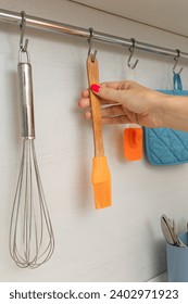 a woman's hand removes a kitchen brush from a hook, vertical photo. kitchen rail for hanging accessories. 
