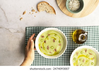 Woman's hand serving creamy green asparagus soup with Iberian ham and olive oil.