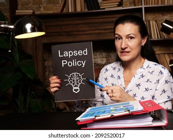 Woman's hand showing black notepad with phrase Lapsed Policy - closeup shot on grey background