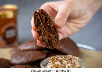 Woman's Hand Showing A Fluffy Thick Chocolate Brownie Cookie Cut In Half. A Bowl Of Peanut Butter Ice Cream And Healthy Homemade Gluten-free Chocolate Chip Cookies In The Background