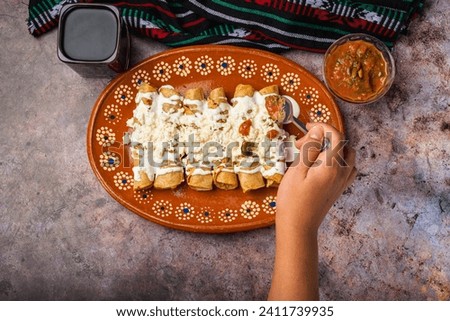 Woman's hand spooning salsa on a plate of golden potato tacos. Mexican food.