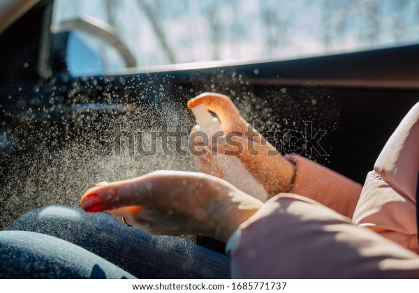 A woman\'s hand\
sprays an antiseptic in the car interior, prevents infection with\
the Covid-19 virus, contamination with microbes or bacteria. Woman\
disinfects her hands.