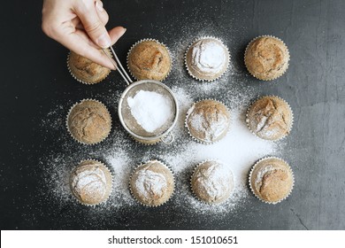 Woman's Hand Sprinkling Icing Sugar Over Fresh Muffins.