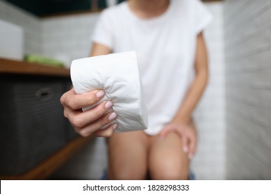 Woman's hand squeezes roll of toilet paper in toilet close-up. Pain during bowel movements proctology concept.