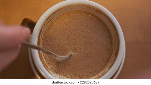 Woman's hand stirs a teaspoon of coffee. Top view, close-up.