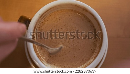 Woman's hand stirs a teaspoon of coffee. Top view, close-up.