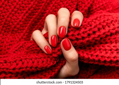 Woman's hand in sweater with red manicure on gray background. Trendy autumn winter nail design. Beauty salon layout