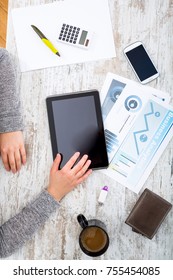 A womans hand at a table useing a tablet.