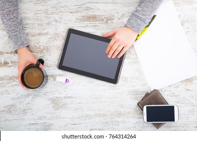 A womans hand at a table useing a tablet.