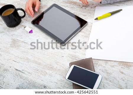 A womans hand at a table useing a tablet.