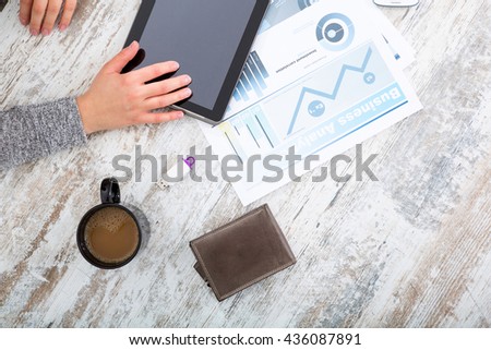A womans hand at a table useing a tablet.