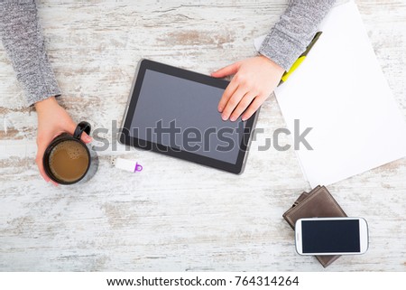 A womans hand at a table useing a tablet.
