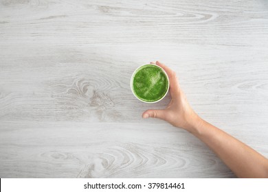 Woman's Hand Takes Away Paper Glass With Prepared Japanese Organic Premium Matcha Tea Latte. On White Wooden Table. Top View