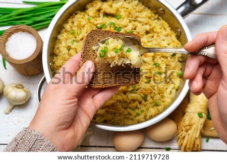 a woman's hand takes fried chopped cabbage in a frying pan, garlic and green onions, cheese, farm eggs and salt, raw and cooked food in a rustic style on a background of white wooden boards