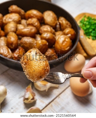 a woman's hand takes fried potatoes from a frying pan, next to other natural products - garlic and green onions, farm eggs and salt, whole cooked food in a rustic style