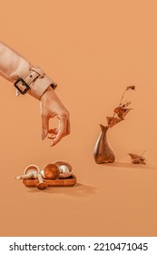 A woman's hand takes ocher mushrooms from a wooden plate. An unusual autumn concept on a Cocha Mocha background. Asymmetric brown vase and dried branch with leaves.Scandinavian style, warm fall tones. - Shutterstock ID 2210471045