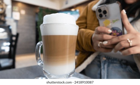 woman's hand takes photo with her cell phone of cup of coffee with foamy milk on table - Powered by Shutterstock