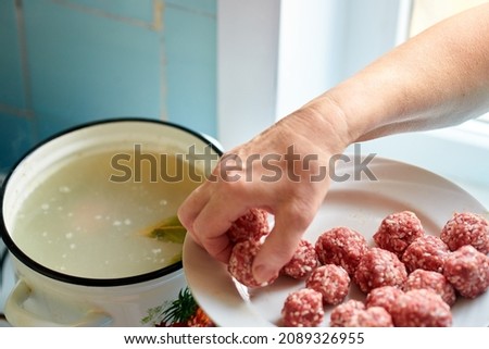 A woman's hand takes raw meatballs from a plate and throws them into a pot of boiling soup. Healthy home cooking.