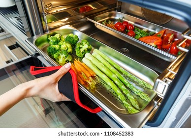 Hand der Frau, die Gemüse auf einem Backblech aus einem Dampfofen herausnimmt