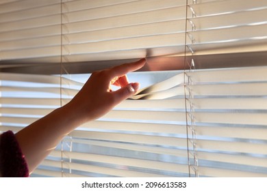 Woman's hand taking a peak through the window blinds. - Shutterstock ID 2096613583