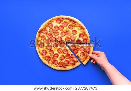Woman's hand taking a slice of freshly baked pepperoni pizza. Homemade pizza minimalist on a blue table