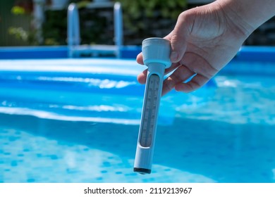 In the woman's hand is a thermometer to measure the temperature of the pool water. In the background is a pool with a blue air mattress - Shutterstock ID 2119213967
