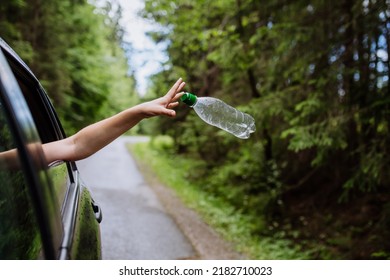 Woman's hand throwing away plastic bottle from car window on the road in green nature, environmental protection, global warming concept