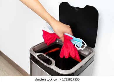Womans hand throws a protective mask and rubber gloves into the trash can on a gray background. End of quarantine concept