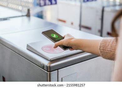 Woman's hand ticking her transport ticket in the machine with her mobile phone on train station. NFC and contactless technology concept - Shutterstock ID 2155981257