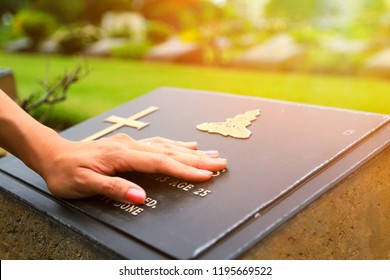 Woman's Hand Touching The Black Stone Grave At Cemetery With Orange Sunlight Flare - Reminisce, Memory, Miss, Sad And Lose Person In The Family Or Important People Concept