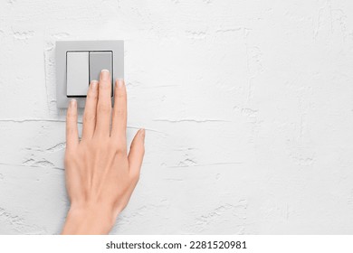 a woman's hand turns on or off the light with a light switch on a gray wall with copy space