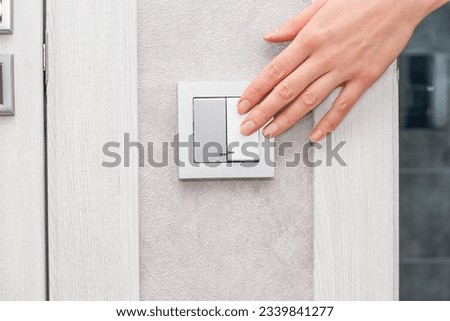 a woman's hand turns on or off the light in the bathroom with a switch on a gray wall