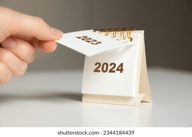 a woman's hand turns over a calendar sheet. year change from 2023 to 2024