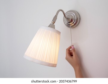 A woman's hand turns the wall sconce on and off with a rope. Night light above the bed - Shutterstock ID 2037436799
