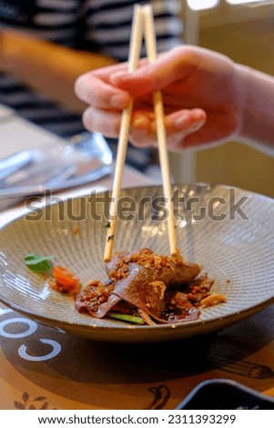 Woman's hand using chopsticks to eat Australian striploin beef spicy Thai salad