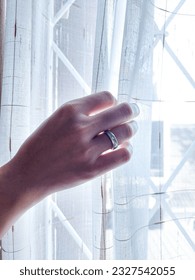 a woman's hand wearing a ring while holding a curtain