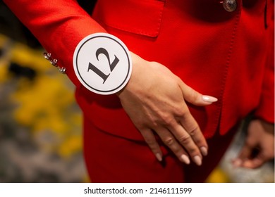  A Woman's Hand Wearing A Wristband With A Number In Order To Go On Stage During A Beauty Contest. Presentation Of A Woman's Suit At A Fashion Show.