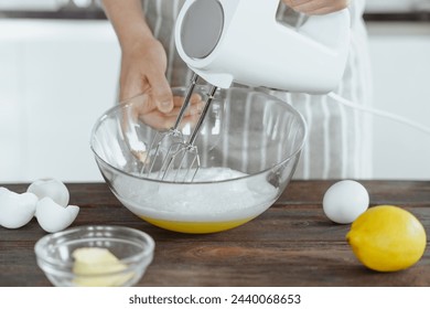 Woman's hand is whisking with eggs white with electric mixer in glass bowl, bakery recipe, kitchen background - Powered by Shutterstock