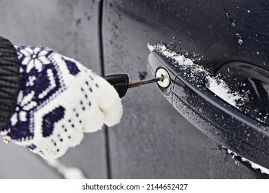 Woman's hand in a winter glove locks the car door lock with a key closeup