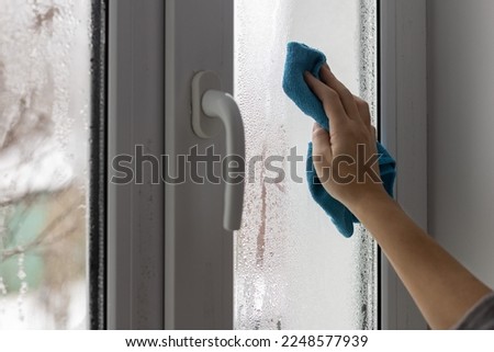 A womans hand wipes the condensate from the window glass with a towel.