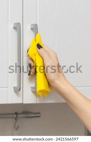 a woman's hand wipes the handle of a kitchen cabinet with a rag. woman wiping kitchen cabinet. kitchen furniture care