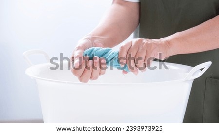 A woman's hand wringing a rag for cleaning,
Hands of a woman squeezing laundry
