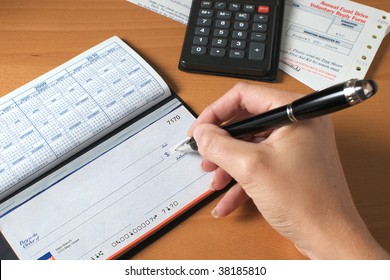 Woman's hand writing a check to pay the bills, with calculator and an invoice on the desktop.