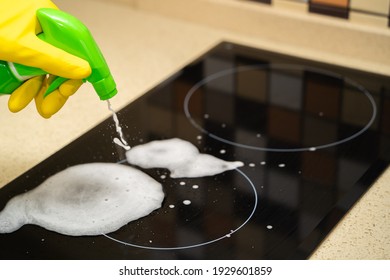 A Woman's Hand In A Yellow Glove Splashes Detergent Onto An Induction Cooker. Closeup Of Unrecognizable Woman Cleaning Glass Ceramic Stove Top.