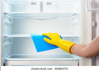 Woman's Hand In Yellow Rubber Protective Glove Cleaning White Open Empty Refrigerator With Blue Rag 