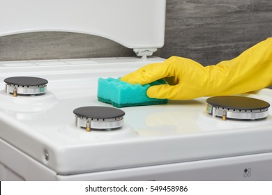Woman's hand in yellow rubber protective glove cleaning white gas stove with green sponge on gray background - Shutterstock ID 549458986
