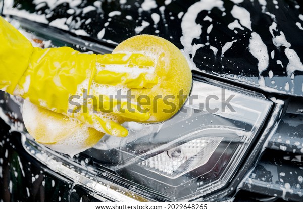 A woman\'s hand with a yellow sponge for washing,\
washing a car.