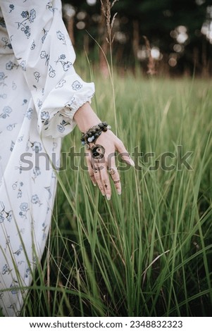 Woman's hand with a yin yang sign and bracelets with magic stones touches the grass.The way to the harmony of the soul