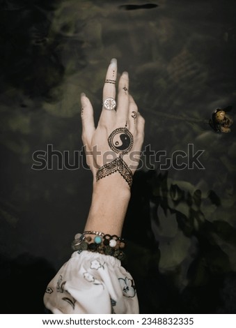 Woman's hand with yin yang sign and bracelets with magic stones underwater. Mehendi pattern